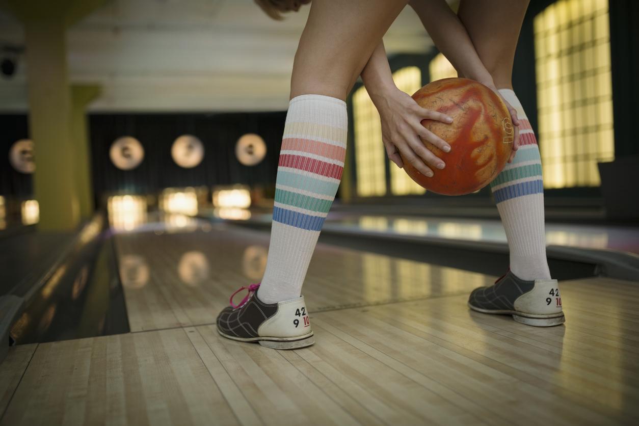 Bowler standing at foul line with striped bowling socks and shoes visible